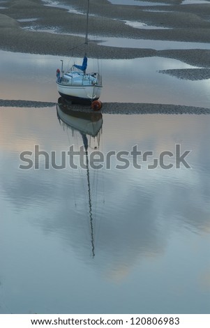 Small sail boat, stuck on mud flat/ Going no where/Tide is receding along the mud flats of North Wales, hampering activity from this anchored sailboat as the sun colors reflect in water.