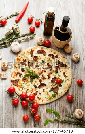 Pizza with mushrooms on a background of red wine, olive oil, cherry tomatoes, mushrooms and herbs.