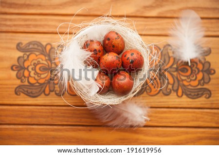 Easter eggs in a basket with a small decorative feathers on background wooden decorative ornament.