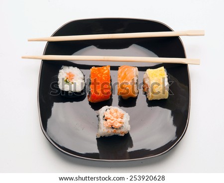 sushi rolls sushi rolls. lie on a black plate five skates and sticks. Photo on a white background.