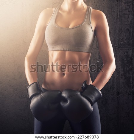 Fitness woman showing strong abs with boxing gloves on her hands