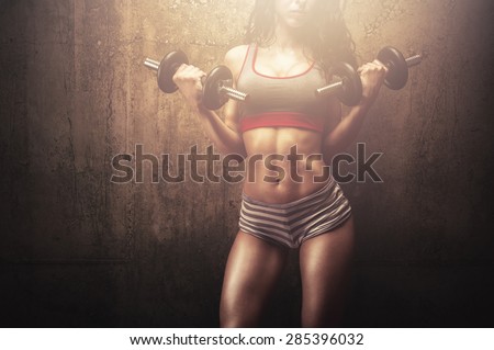 Fitness young woman in hard training building muscles and posing in front of gym wall