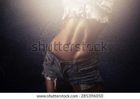 Shaped young woman showing perfect tanned and fit belly exposing perfectly sculpted abs