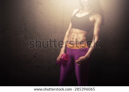 Young fitness woman posing with protein shake bottle showing her perfect sculpted muscular and tight body