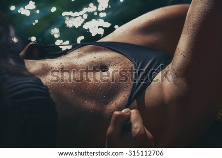 Strong woman abs with water drops on the sun by the sea