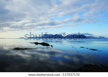 Beautiful scenic landscape - dramatic cloudy sky reflected at calm blue water against the background of distant rugged mountain range, Spitsbergen archipelago (Svalbard island, Norway), Greenland Sea