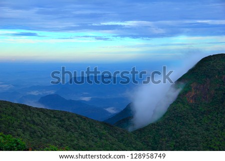 Beautiful scenic view from the Sri Pada (Adam's Peak) at morning with shadow figures of fogged mountain tops against the background of dramatic blue sky at sunrise time, Sri Lanka island, South Asia