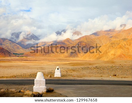 Beautiful view two sign posts stay opposite one another on lonesome road against the background of distant colorful mountain range and dramatic cloudy sky in Ladakh, Jammu & Kashmir, Northern India