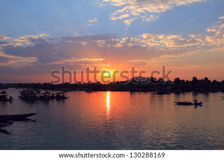 Amazing scenic view - colorful sunset with dramatic cloudy blue sky above calm water of Dal Lake and traditional boat (shikara) shadow figures, Srinagar, Jammu & Kashmir, Northern India, Central Asia