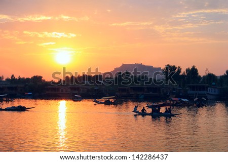 Beautiful scenic view - colorful sunset above calm water of Dal Lake with dramatic cloudy sky and traditional boat (shikara) shadow figures, Srinagar, Jammu & Kashmir, Northern India, Central Asia