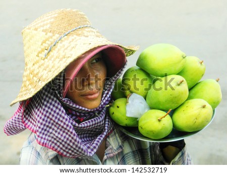 PHNOM PENH/CAMBODIA - MAY 09. Young woman dressed in a straw hat and check scarf carries plate with green mango for sale on may 09, 2013 in Pnom Penh central market, Cambodia, South East Asia