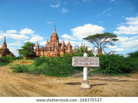 Beautiful scenic view - ancient Hindu Temple, country road fork and burmese city sign board against the background of cloudy blue sky in Bagan, Myanmar (Burma), South East Asia