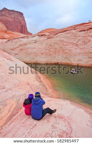 Two hikers sitting on the edge of cliff overlooking Lake Powell, Arizona, USA