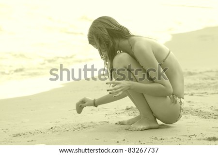 Vintage styled portrait of beautiful teenage girl, drawing on sand by the sea