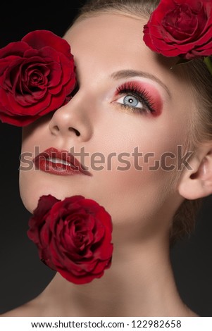 close-up portrait of blonde girl with three red roses near the face, she is turned of three quarters and looks up
