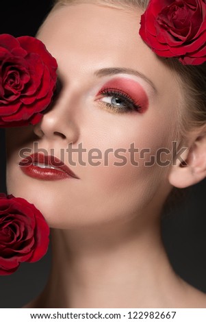 close-up portrait of blonde girl with three red roses near the face, she looks in to the lens with sensual eyes