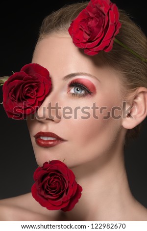 close-up portrait of blonde girl with three red roses near the face, she is turned of three quarters and looks in front of her
