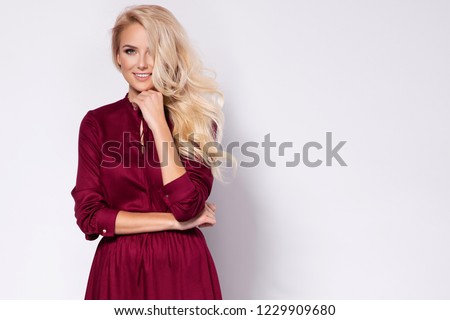 Fashion photo of a beautiful blonde young woman in a pretty dress, red hat holding handbag posing over white background. Fashion autumn summer photo. Hairstyle