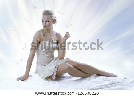 pretty blonde girl with elegant dress sitting on white floor, with a sky as a background Her face is turned of three quarters at right and she looks down