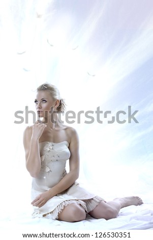 pretty blonde girl with elegant dress sitting on white floor, with a sky as a background , she looks up at right and her right hand is near the chin