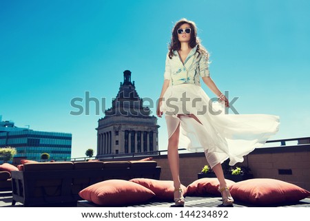 Beautiful Woman White Loose Skirt, High Heels, And Jeans Jacket Standing On The Bed On The Rooftop