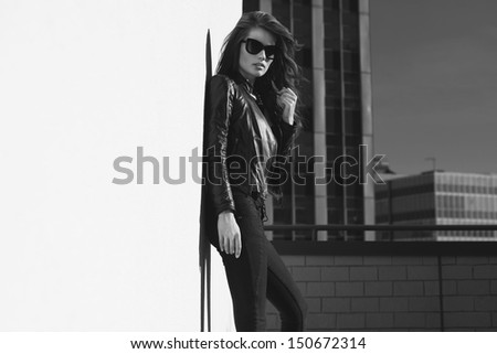 Glamorous young woman in black leather jacket and sunglasses on the rooftop