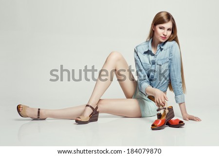 Glamorous blonde woman sitting in the studio presenting summer shoes