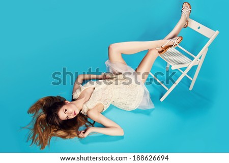 young blonde woman posing on a chair in white laced dress