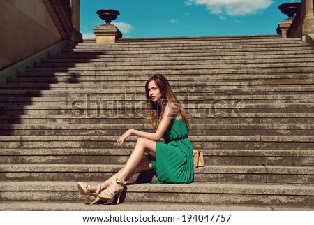 beautiful young woman in fashionable green dress standing on stairs