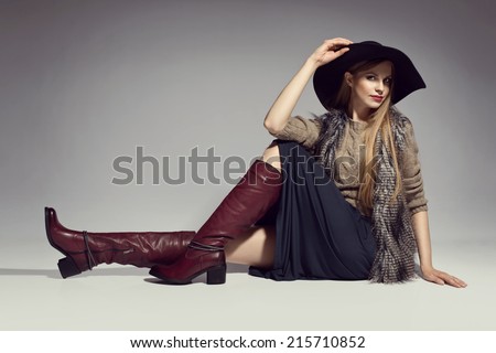 Fashionable woman in a hat, boots and autumn clothes, posing in studio