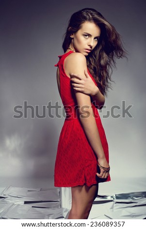 Beautiful brunette young woman in elegant evening red dress. Posing on shining mirror floor
