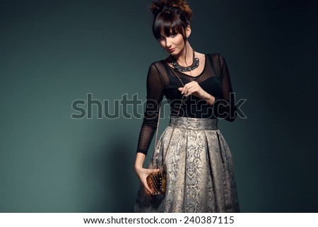 Fashionable young woman in elegant golden skirt and black transparent top, holding evening handbag. Glamour style