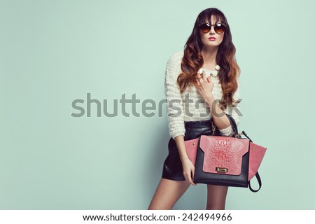 beautiful young woman posing in sunglasses, leather shorts, handbag and sweater