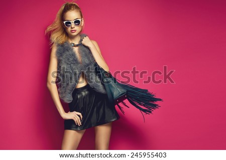 Stylish beautiful blonde woman wearing feather vest holding nice big fringed handbag. Fashion picture