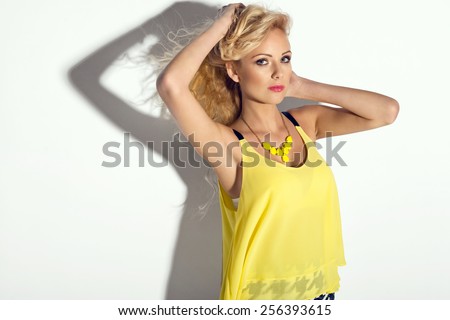 Wonderful young blonde woman in fashionable summer clothes with long wavy hair looking at camera, high heels shoes