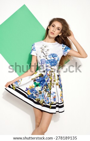 beautiful young brunette woman in nice colorful summer dress, high heels, handbag, long hair posing in studio. Fashion photo