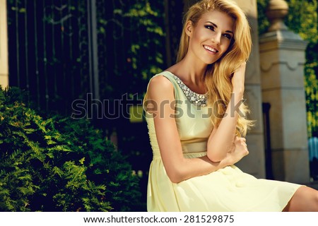 Beautiful blonde young woman wearing yellow summer dress, posing in the parc