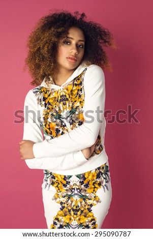 Beautiful African American woman posing in nice flower pattern skirt and white hoodie on a pink background. Fashion photo with afro hairstyle.