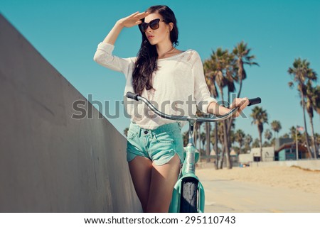 Outdoor portrait of happy woman biking in city park. Joy and happiness. Young woman in shorts, sunglasses on holidays. Venice, Los Angeles.