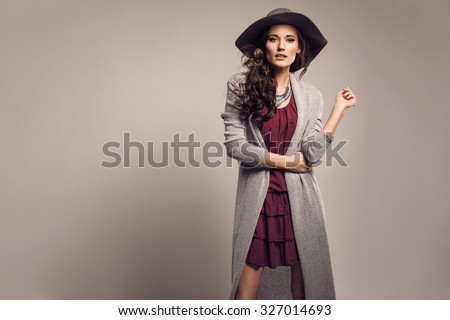 Fashionable woman in a hat, dress and long grey sweater, accessories, high heels, posing in studio. Fashion autumn photo
