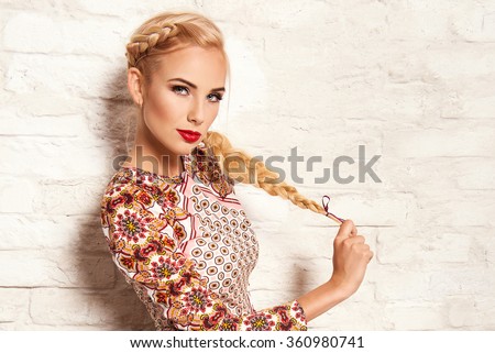 beautiful young blonde woman in nice spring dress, posing on white brick wall. Fashion photo, folklore style. Braid hair style