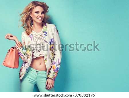 Beautiful woman wearing nice clothes, handbag posing on turquoise background. Fashion spring photo