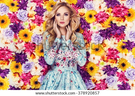 Beautiful young woman in nice blue dress posing on colorful wall of flowers. Fashion photo, nice hair, big smile