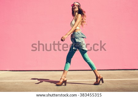 Sexy young woman walking in a city next to pink wall in jeans shirt and mint pants. Fashion summer photo