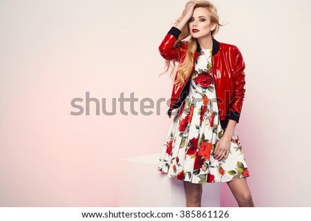 beautiful young blonde woman in nice spring dress and red plactic jacket posing in a studio. Fashion photo