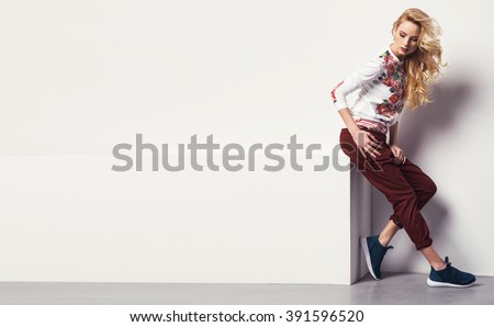 beautiful young blonde woman in a sweatshirt flower with pattern and jeans posing in studio. Fashion photo