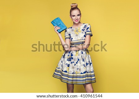 beautiful young blonde woman in nice spring dress, posing on yellow background in studio. Fashion photo, purse