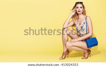 beautiful young blonde woman in nice summer clothes, posing on yellow background in studio. Fashion photo, handbag, high heels shoes