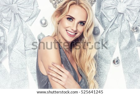 Beautiful young elegant woman in sexy silver dress posing over white background with glitter ribbons christmas balls holding present. Christmas photo