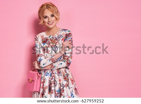 Fashion photo of a beautiful elegant young woman in a pretty dress with flowers holding handbag posing over pink background. Fashion spring summer photo